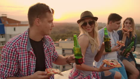 Loving-young-couples-sit-on-the-roof-and-drink-beer-with-pizza.-They-enjoy-a-beautiful-sunset-and-time-with-their-mates.